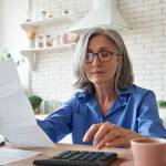Senior mature business woman holding paper bill using calculator.