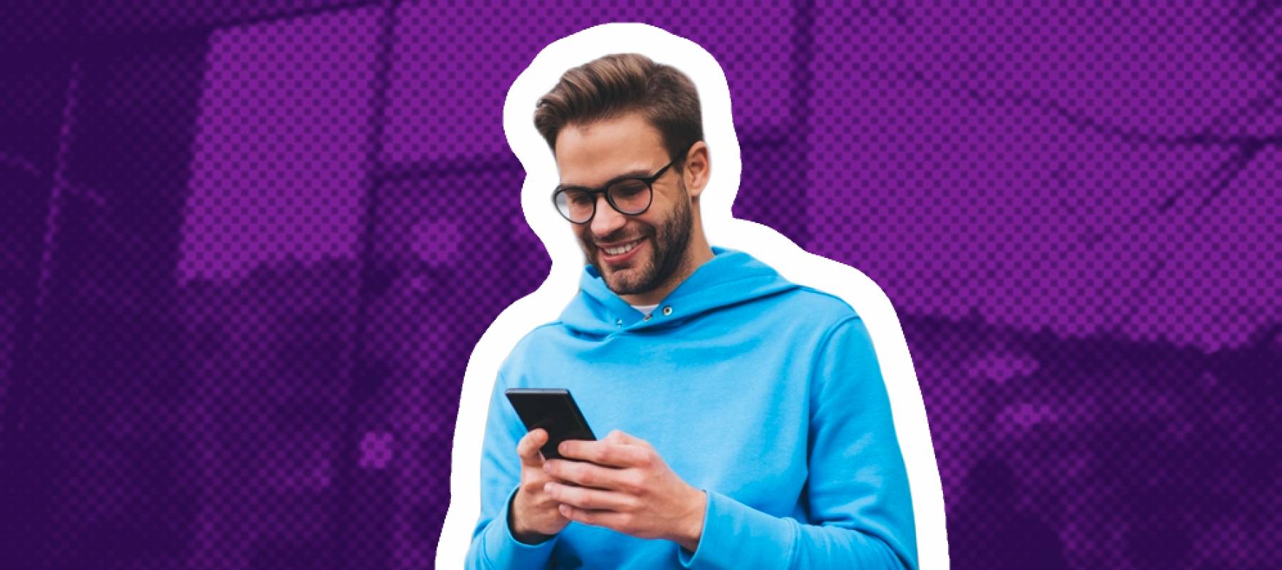 Happy young man sits on a bench outside, looking down at his phone.