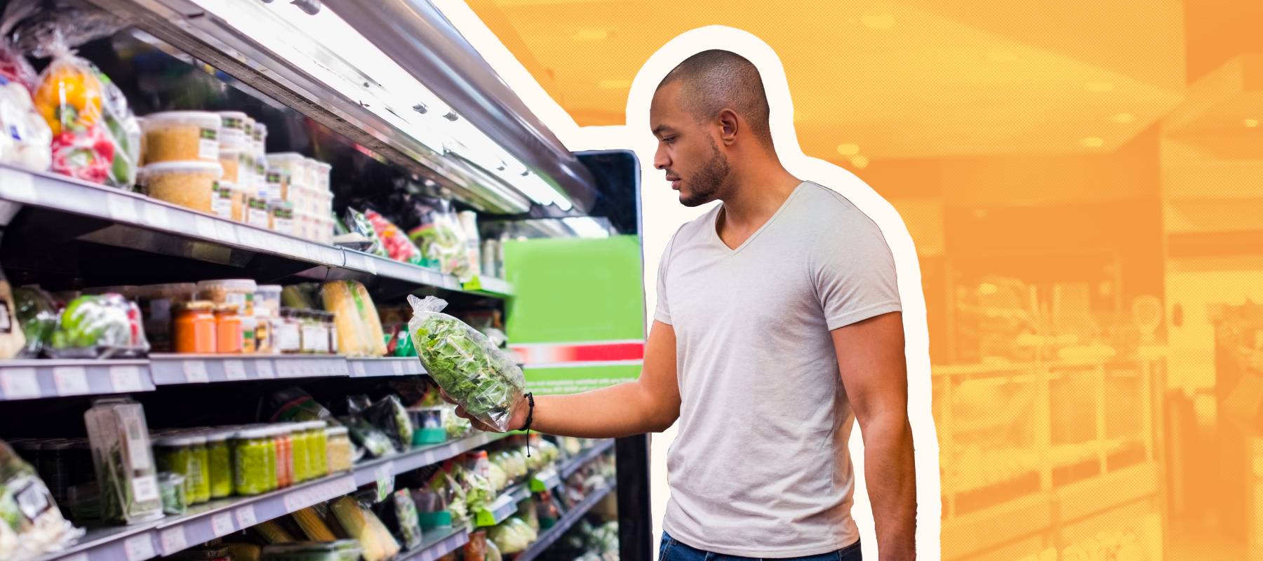 Man stands in produce aisle at grocery store holding a basket and looking at a box of greens.