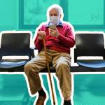 Older man sits wearing a mask in a doctor's office waiting room, looking at his phone.