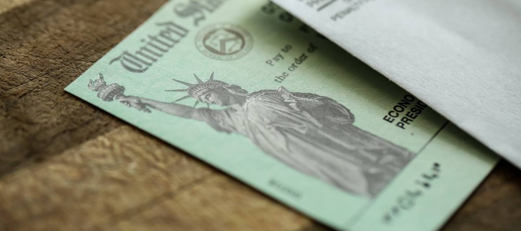 Stimulus check on a wooden table with envelope on top of it.