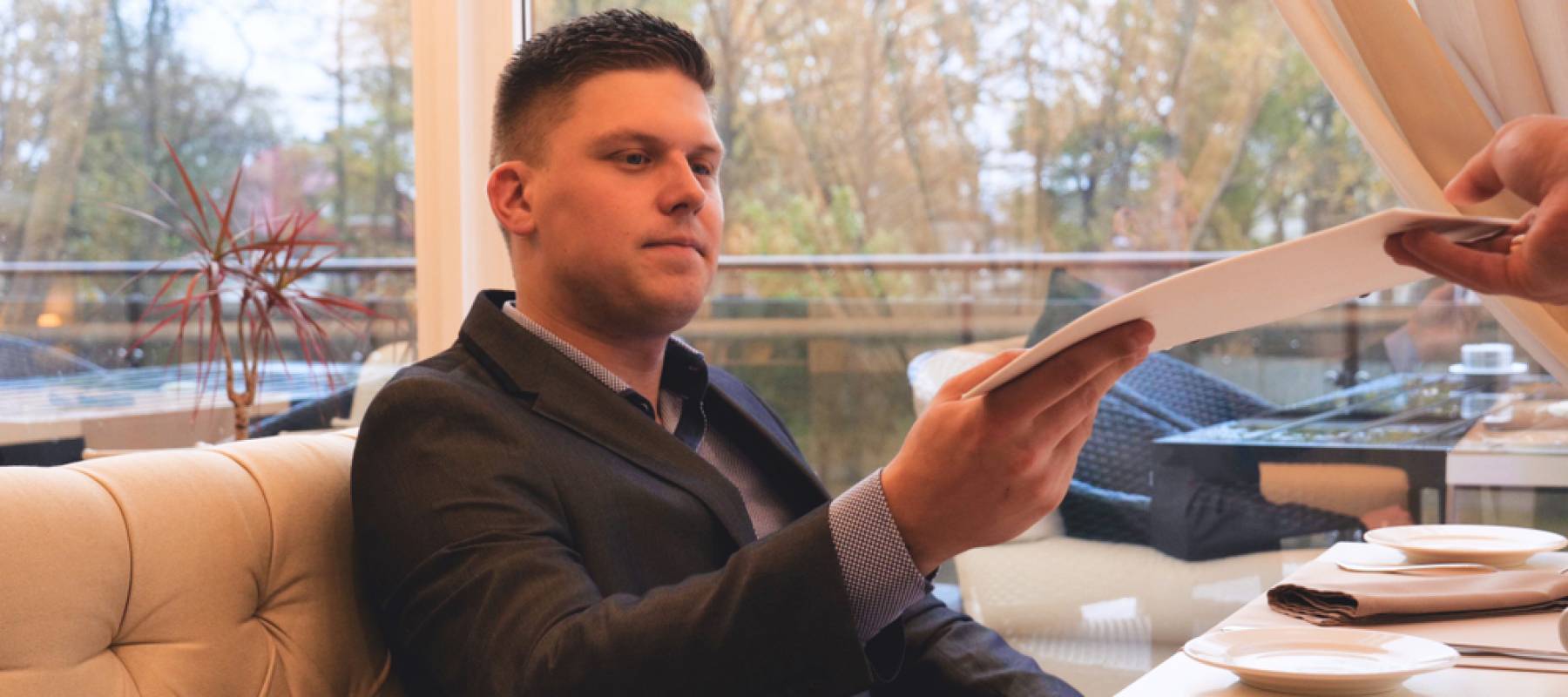 Man sitting in booth at restaurant takes menu from server.
