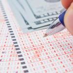 Male's hand marking number on lottery ticket. Close-up, selective focus.