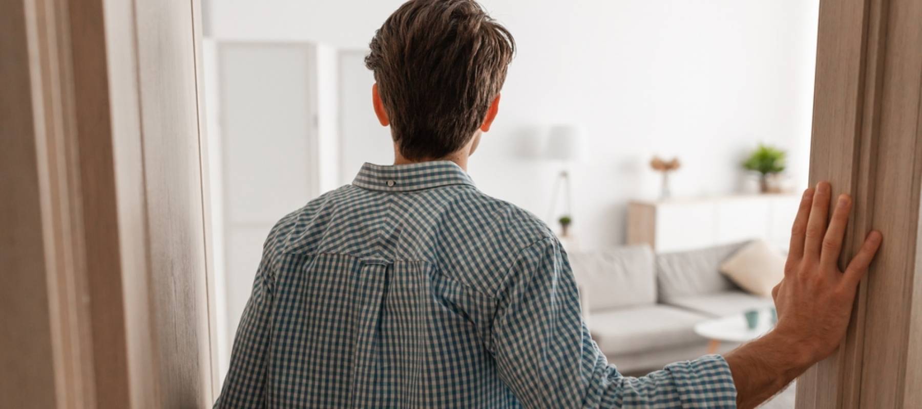 View of man from behind with hand on door frame, looking into a living room.