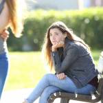 Sad single girl seeing an affectionate couple who are walking outdoors in a park