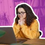 Young woman with hands clasped under her chin looking at laptop.
