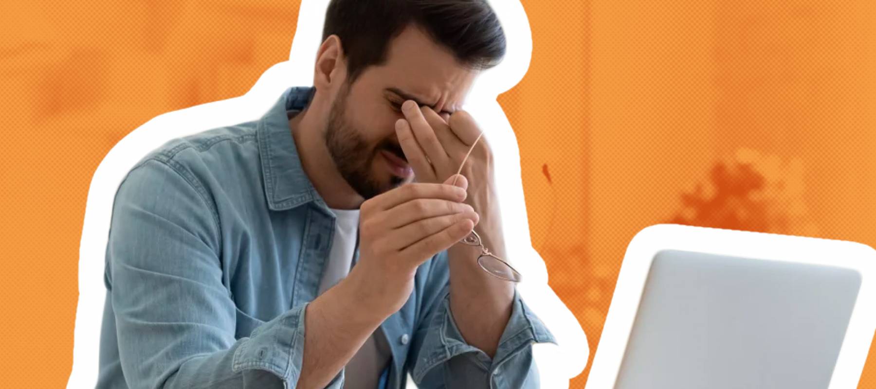 Stressed young man holds face while sitting in front of laptop.