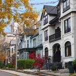 Street of historically designated old Victorian houses with gables and painted brick, downtown Toronto, with large office building in background
