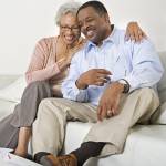 A retirement-aged couple smile on the couch.