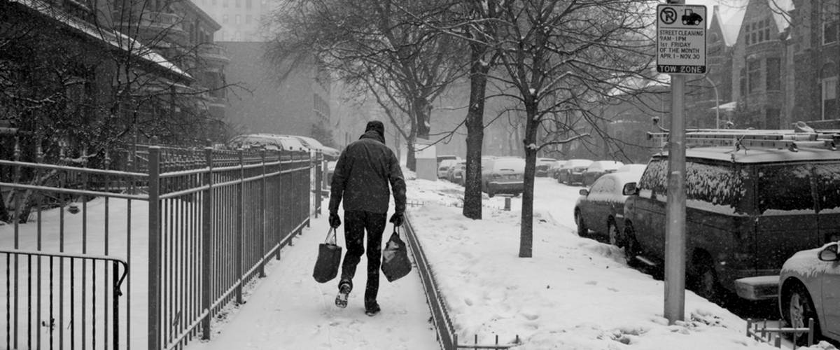 Man walking down a snowy sidewalk with groceries.