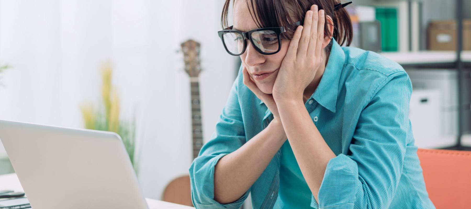 Bored young woman in the office working with a laptop and staring at computer screen