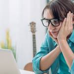 Bored young woman in the office working with a laptop and staring at computer screen