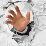 Hand reaches out from big heap of crumpled papers