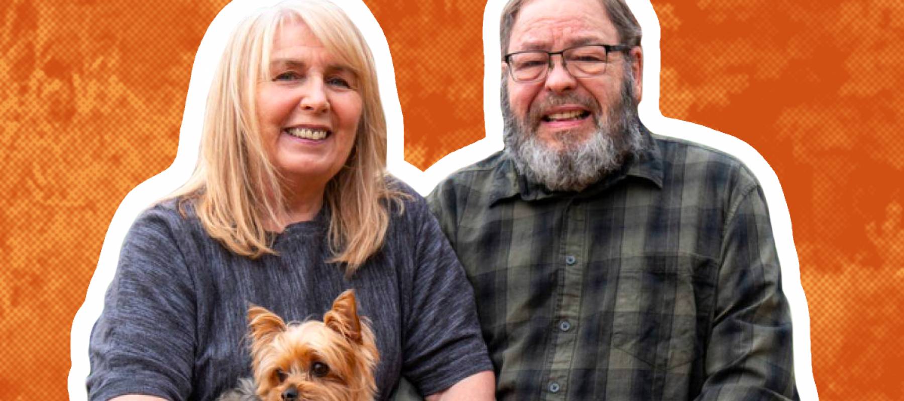 Older couple pose with small dog sitting with pumpkins in a field.