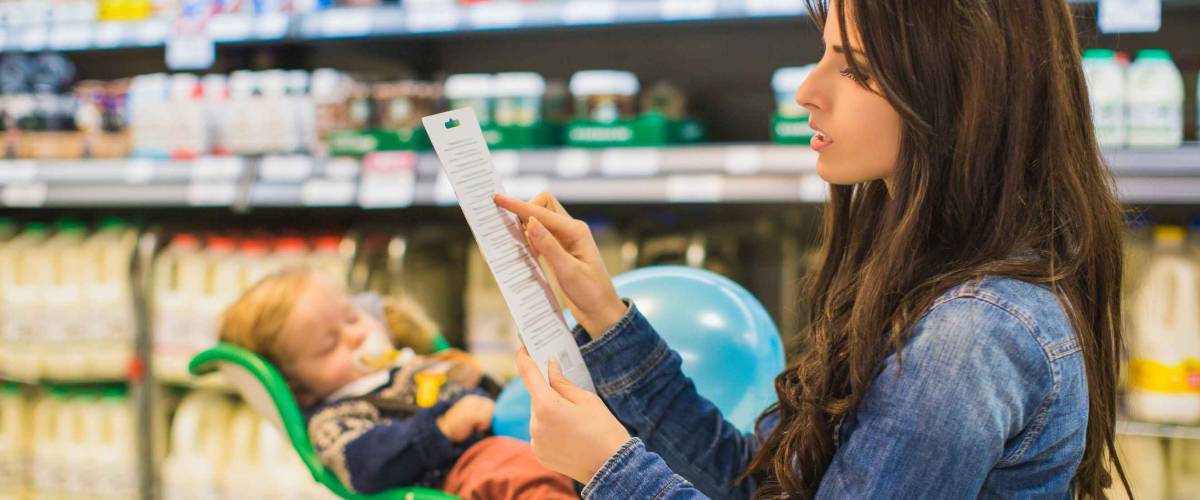 Young woman with a long shopping list in. Little son sleeping in shop