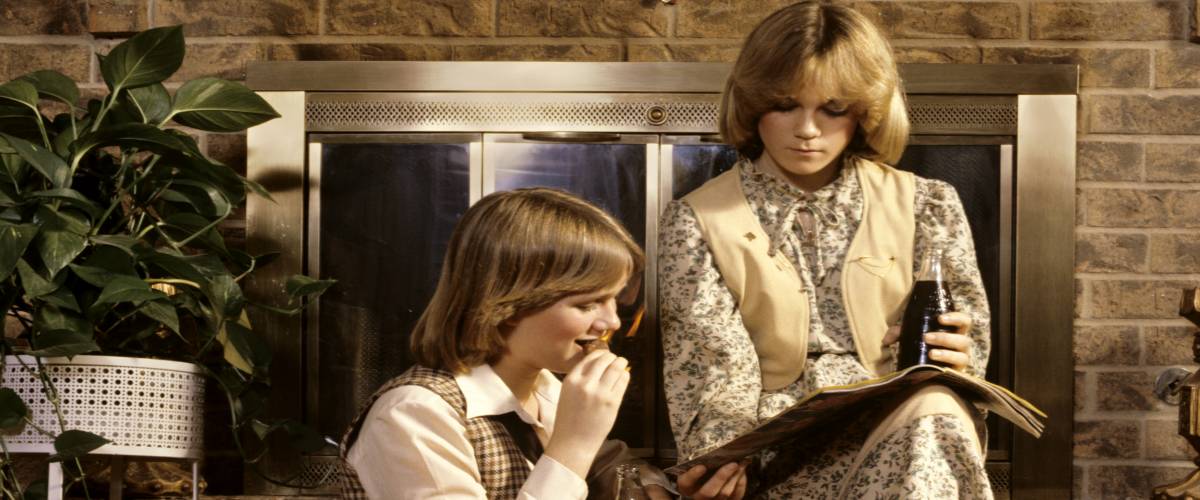 Two 80s teens sitting on a fireplace, reading