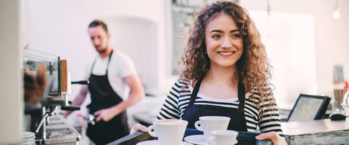 Millennial femme teen, balancing a tray full of dishes, standing in front of a restaurant counter