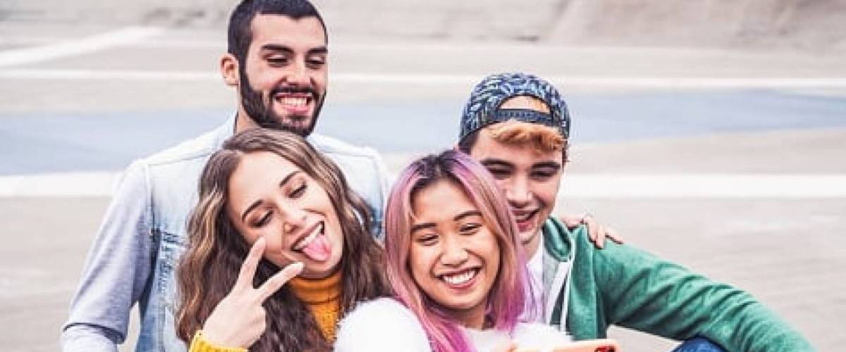 a group of Gen Z teenagers sitting on a beach taking casual photo