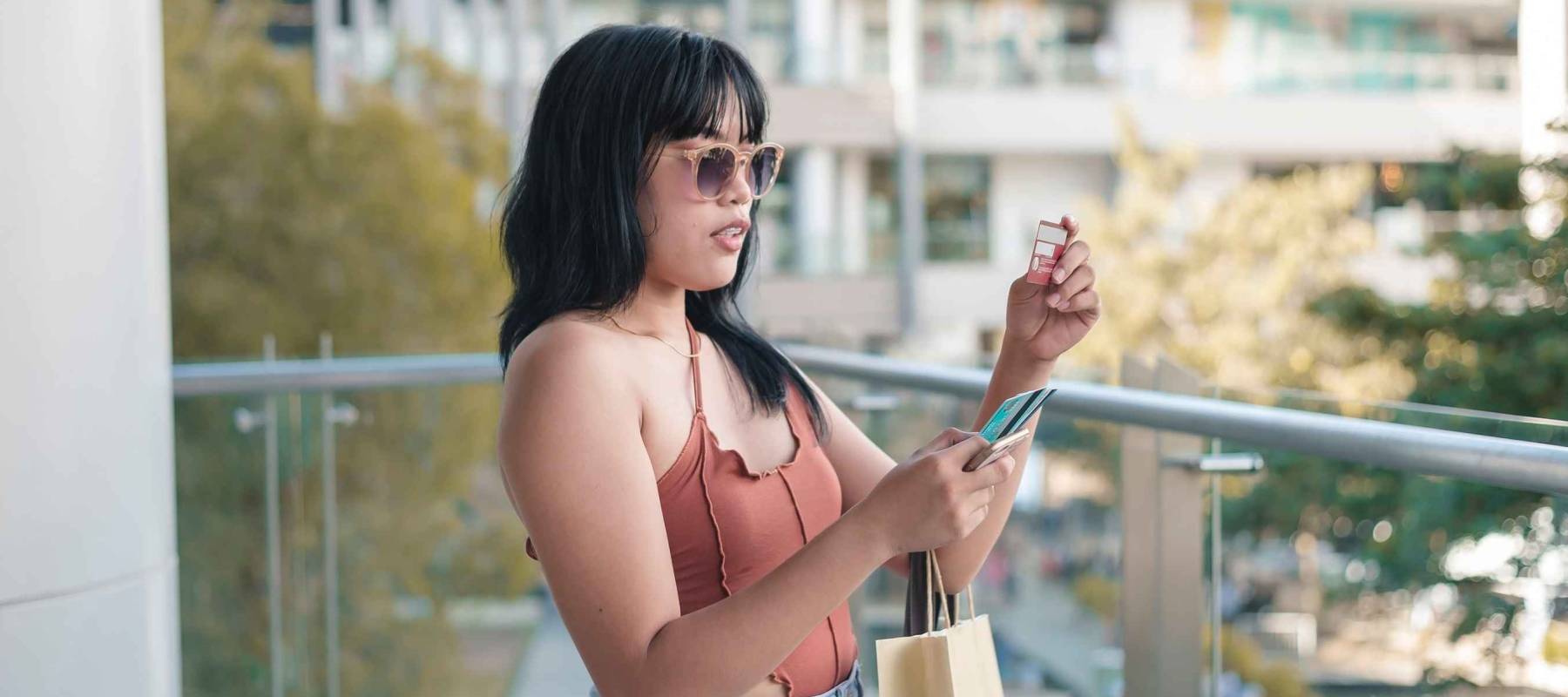 A young lady attempts to input the CVV number of a credit card on her cellphone during an impulsive online transaction. Also doing traditional shopping at the mall.