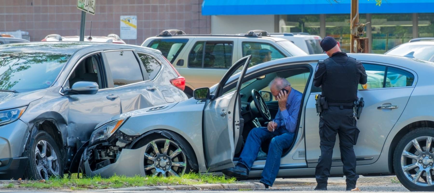 Car accident scene with damaged cars, policeman writing traffic ticket and driver on cell phone.