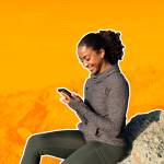 Woman on rocky beach smiling at phone