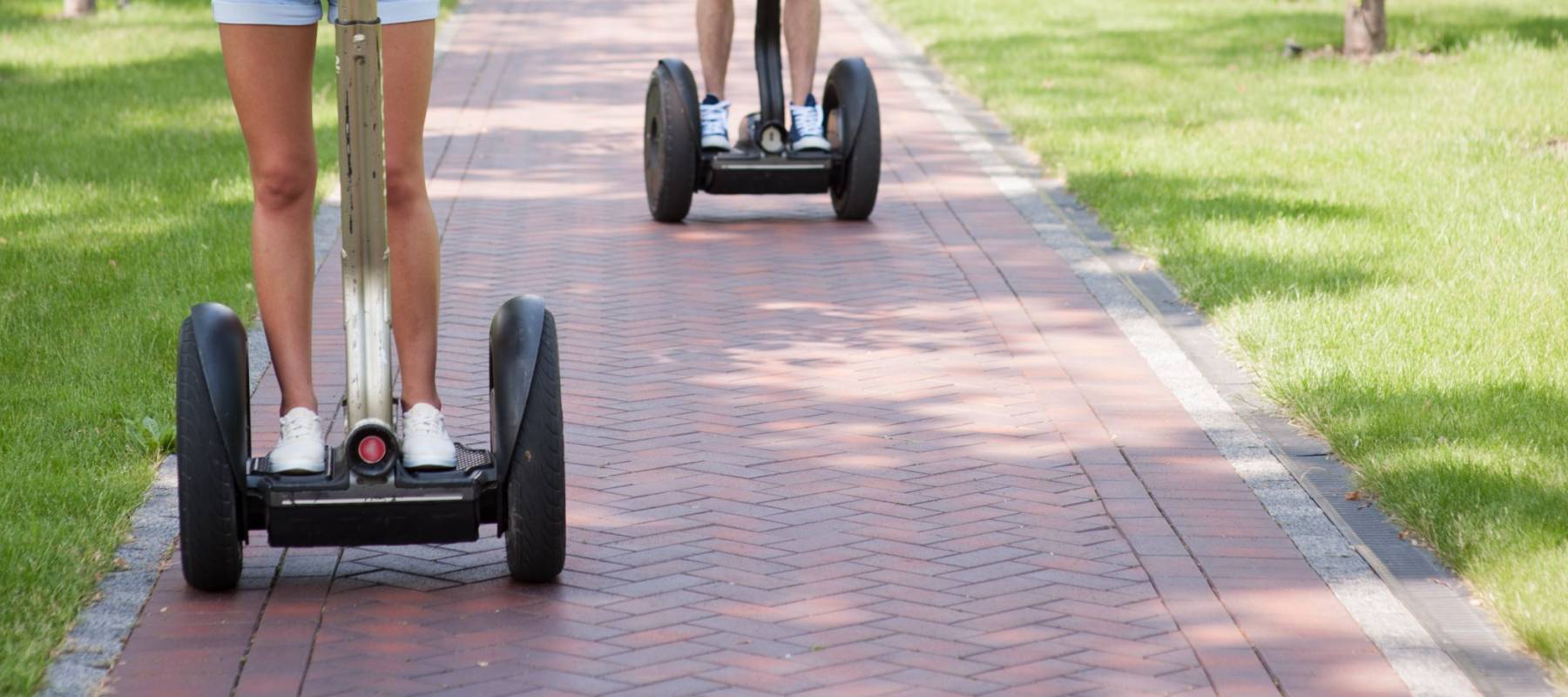 Portrait of beautiful young woman and handsome man. Girl and boy using segway. Girl smiling. Green alley as background