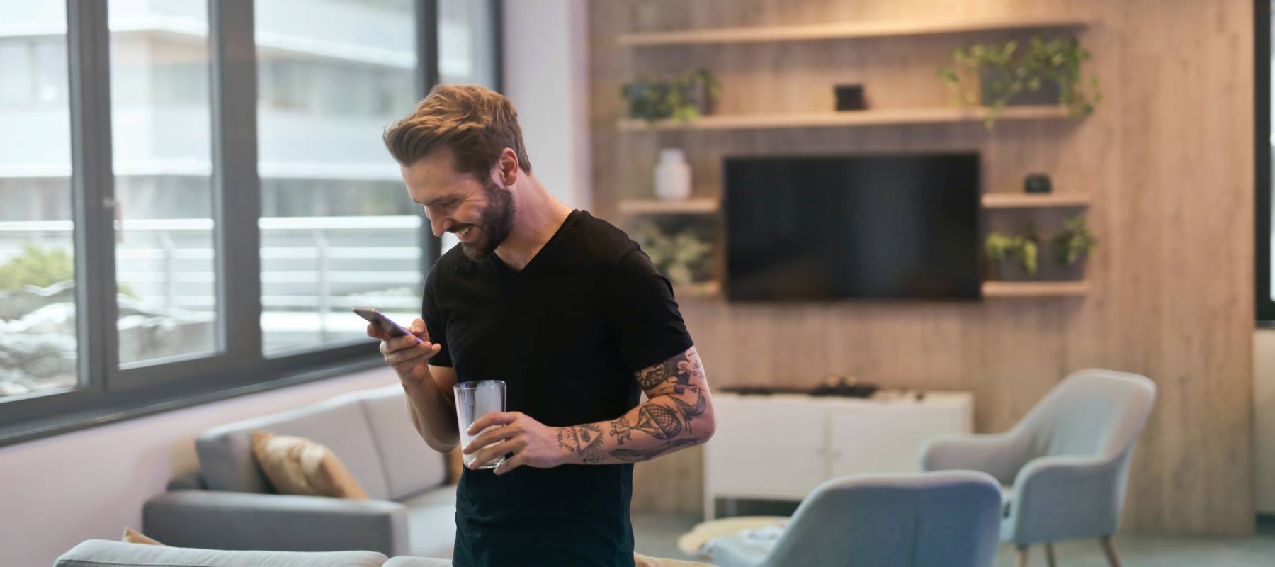 Young man smiling while looking at his phone in nicely furnished apartment