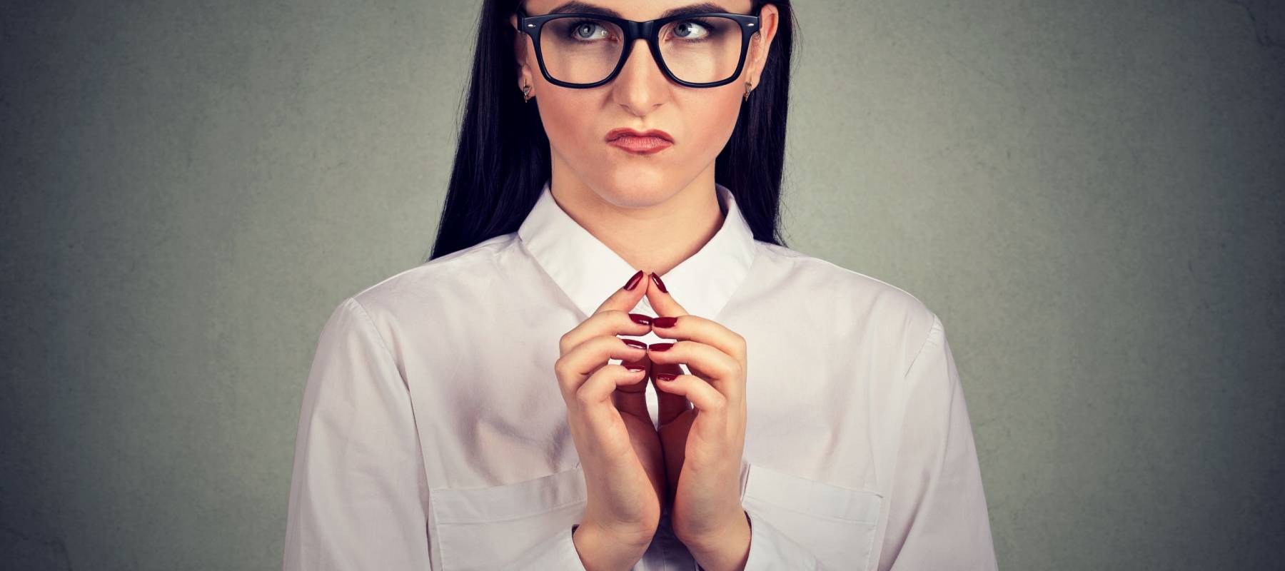 Young sly girl in glasses holding hands together and looking up in thoughts of revenge and jealousy