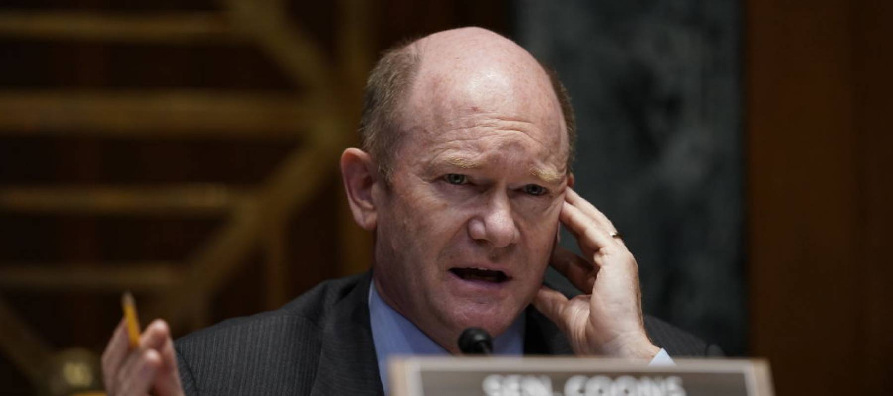 Sen. Chris Coons presses his hand up against his head as he speaks in the Senate.