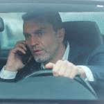 Close up view of stressed middle aged man in a car talking on phone while driving.