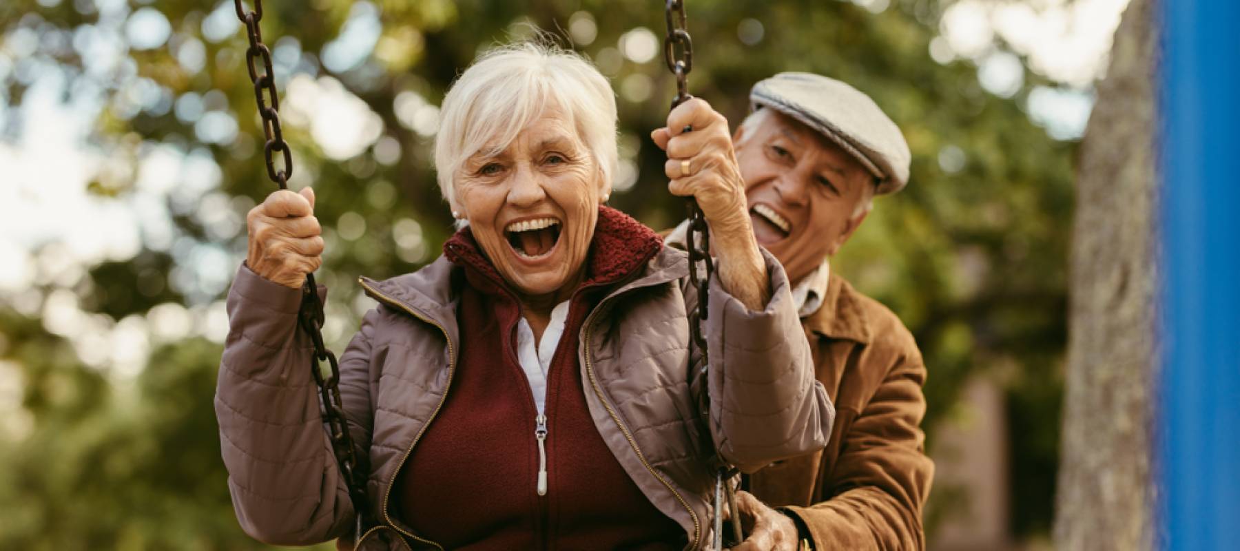 Senior man pushing his female partner on swing in park and having fun together.