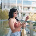 A young lady attempts to input the CVV number of a credit card on her cellphone during an impulsive online transaction while standing on a balcony.