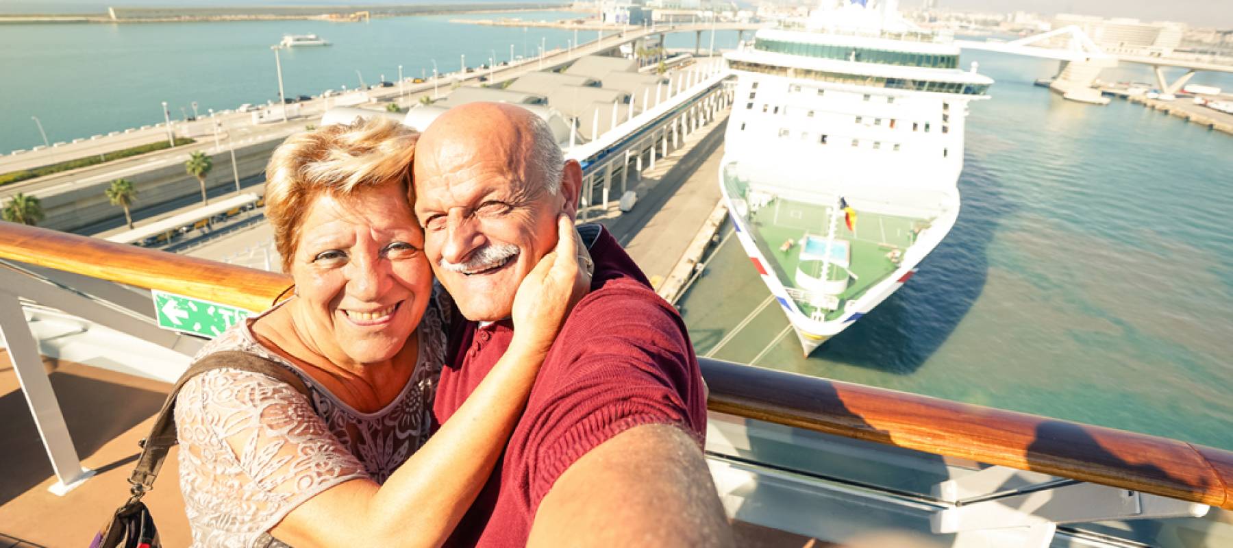 Senior happy couple taking selfie on ship with a harbor in the background.