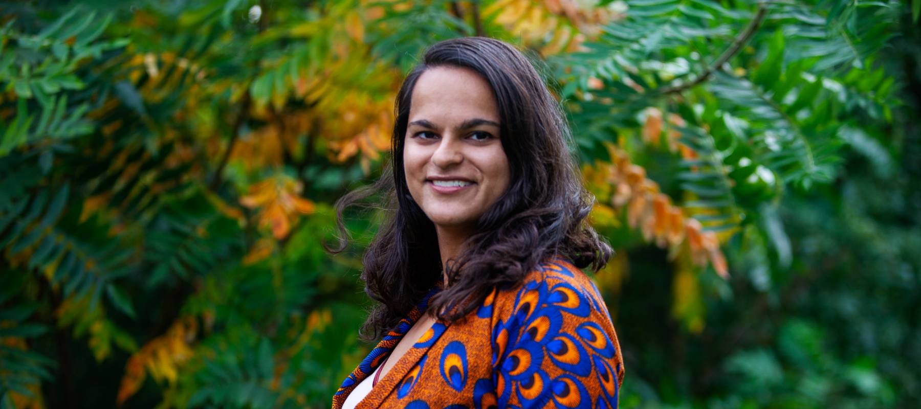 Siobhan Neela-Stock poses outdoors, smiling gently at the camera.