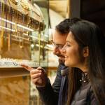 Happy beautiful young couple choosing a wedding rings while smiling and pointing into shop window.