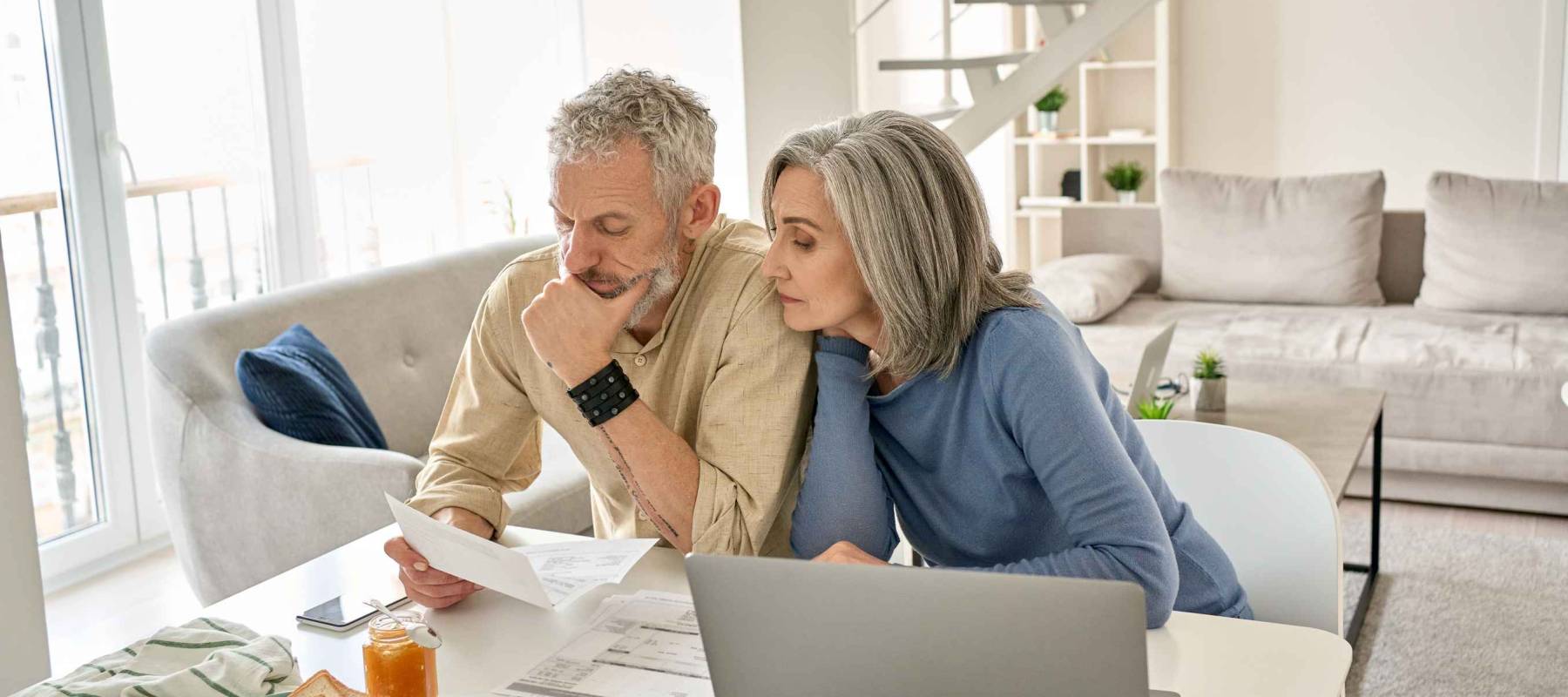 Worried old senior couple checking bank documents at home.
