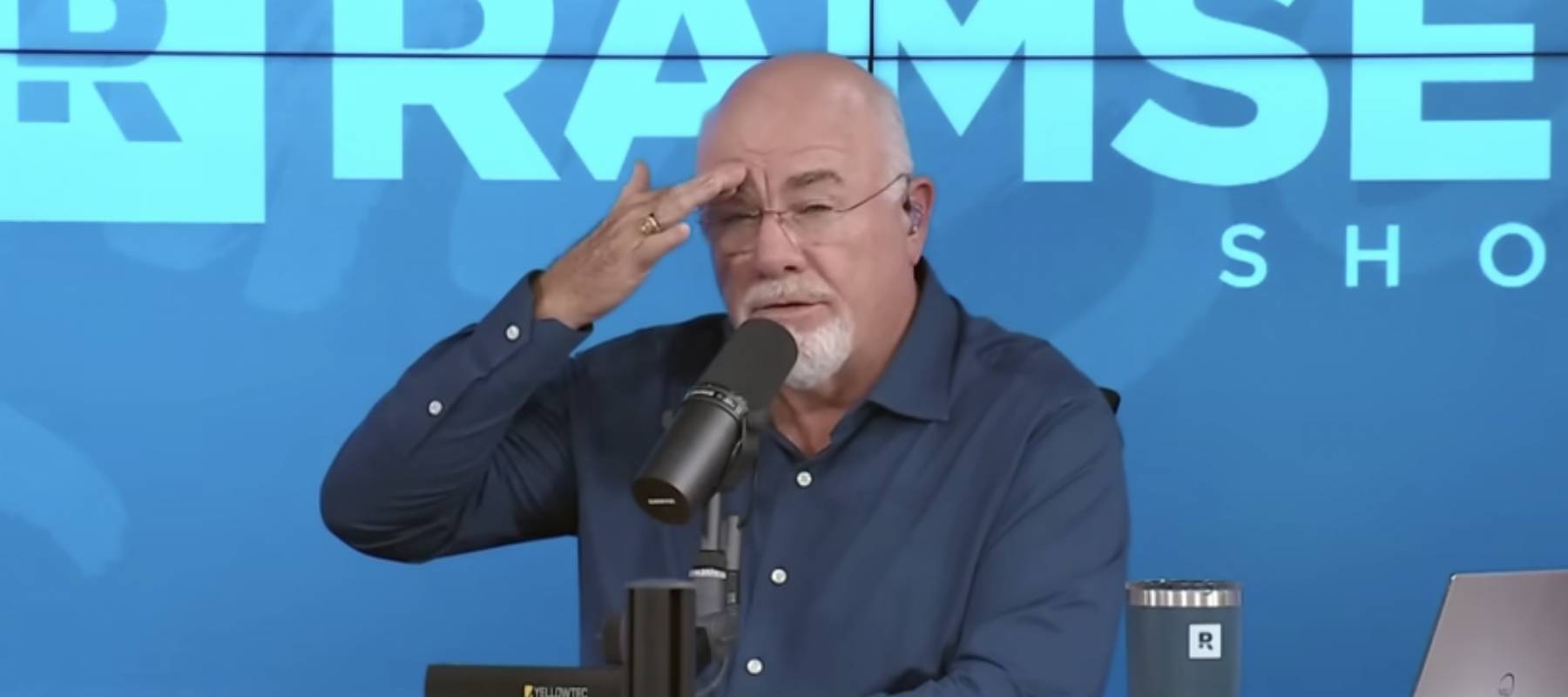 Dave Ramsey speaks on set of his show with his hand on his brow.
