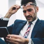 Mature successful entrepreneur dressed in formal wear reading banking notification on smartphone device