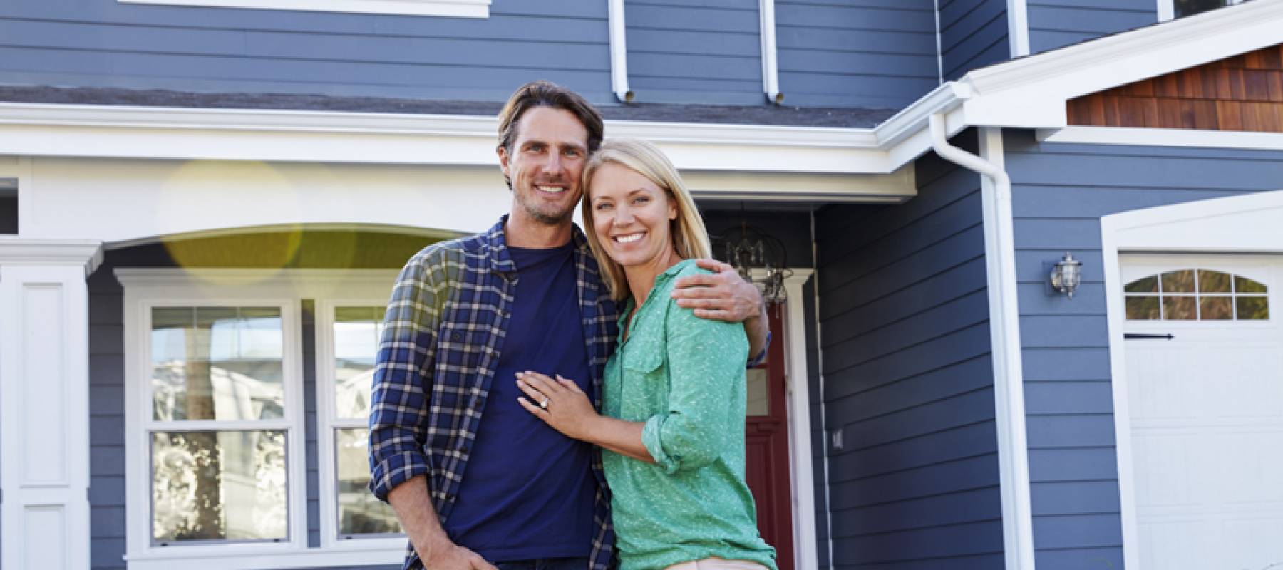Happy couple pose in front of new house, smiling.