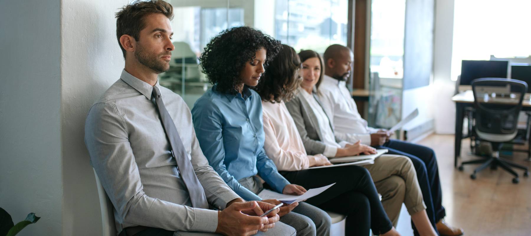 Diverse group of job applicants sitting together outside of an office waiting to be interviewed