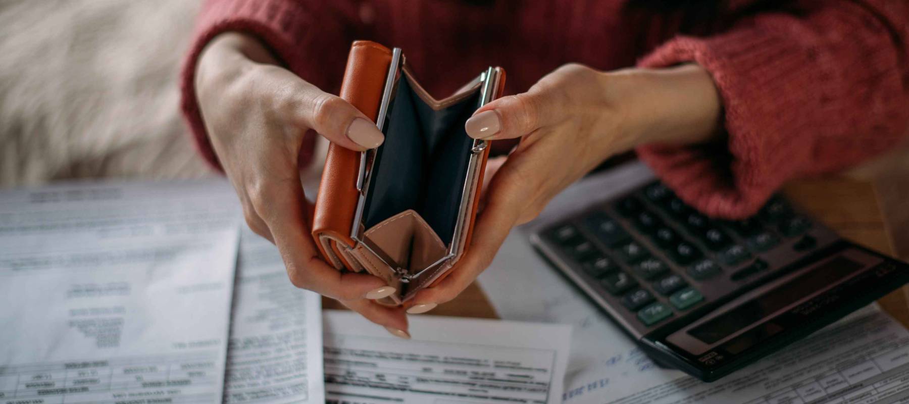 Close-up of woman's hands with empty wallet and utility bills. The concept of rising prices for heating. Many utility bills, coins and hands in a warm sweater holding an open wallet