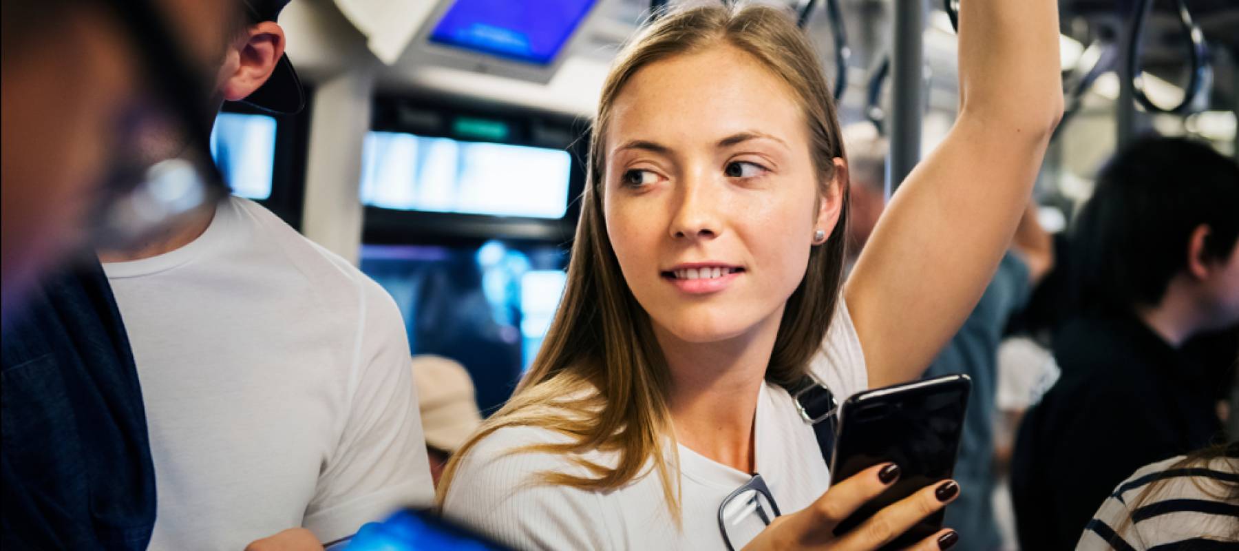 Young woman standing on subway, looking to the side while holding her phone.