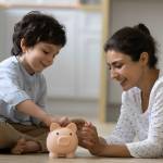 Happy Indian kid and young mom saving money together, putting cash into ceramic piggy bank. Teaching child to invest money, planning future