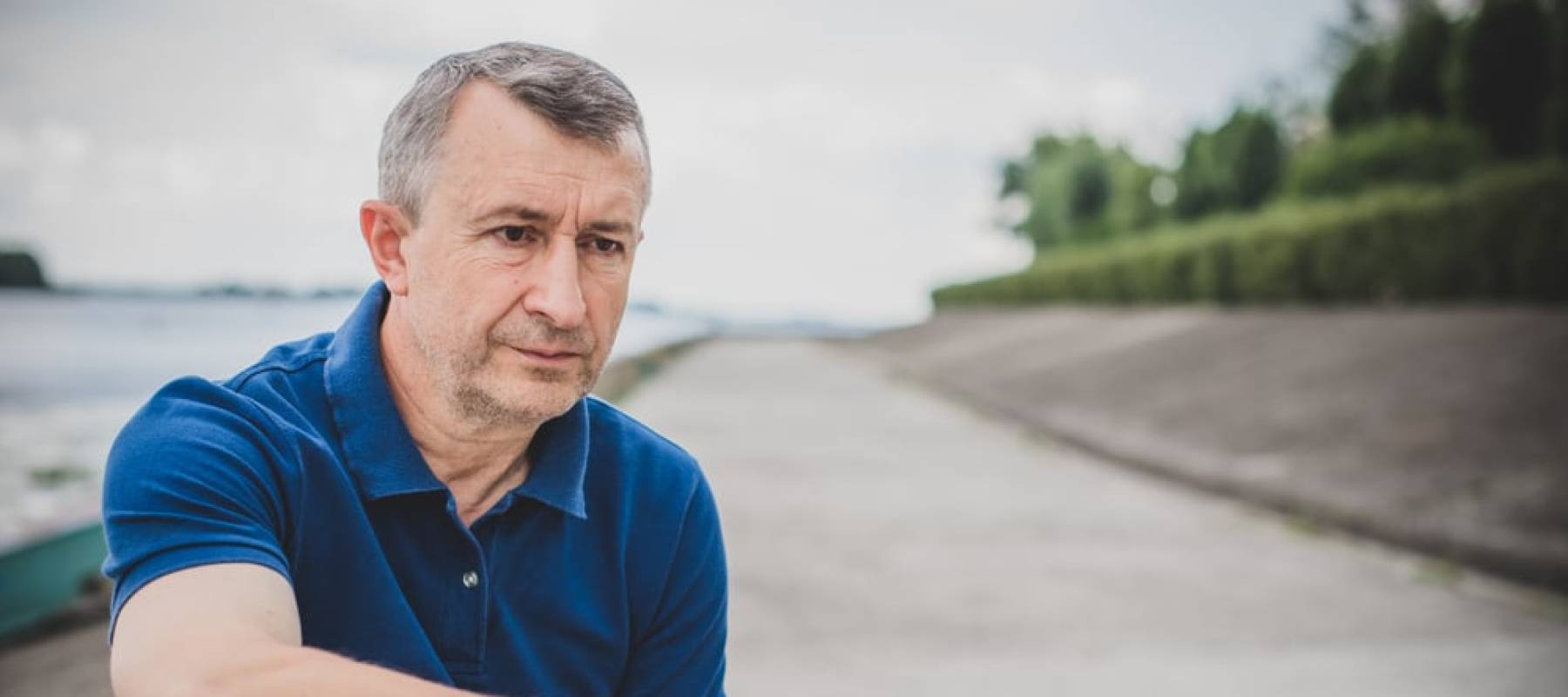 Older man sits on bench outside, looking mournful.