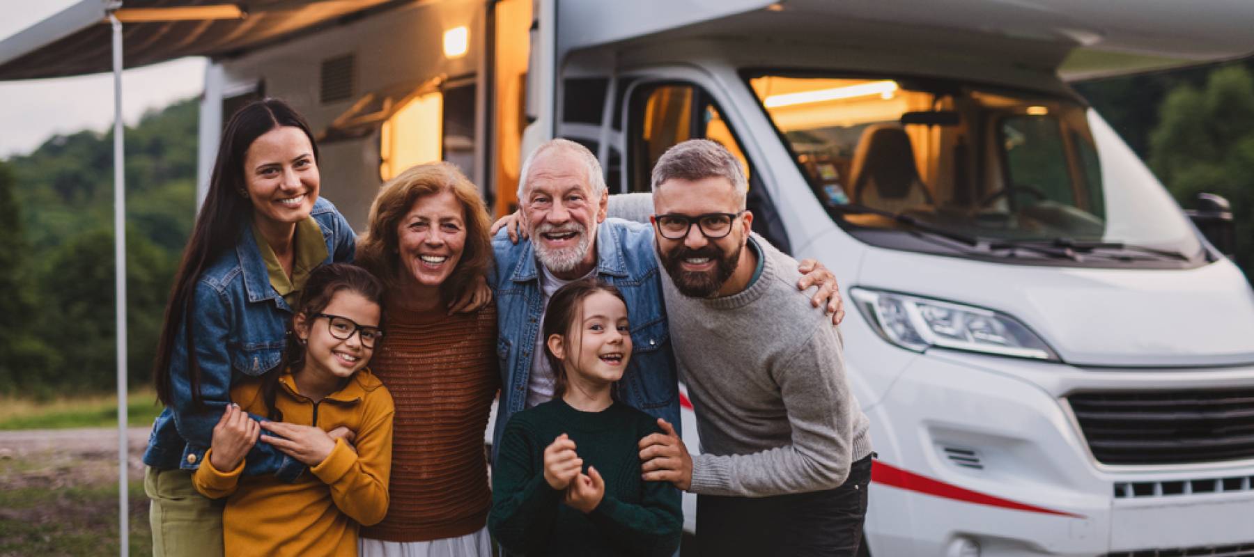 Multi-generation family looking at camera outdoors at dusk, caravan holiday trip.