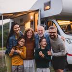 Multi-generation family looking at camera outdoors at dusk, caravan holiday trip.