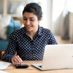 Happy millennial Indian girl sit at desk in living room