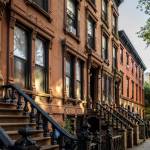 Scenic view of a classic Brooklyn brownstone block with a long facade and ornate stoop balustrades on a summer day in Clinton Hills, Brooklyn