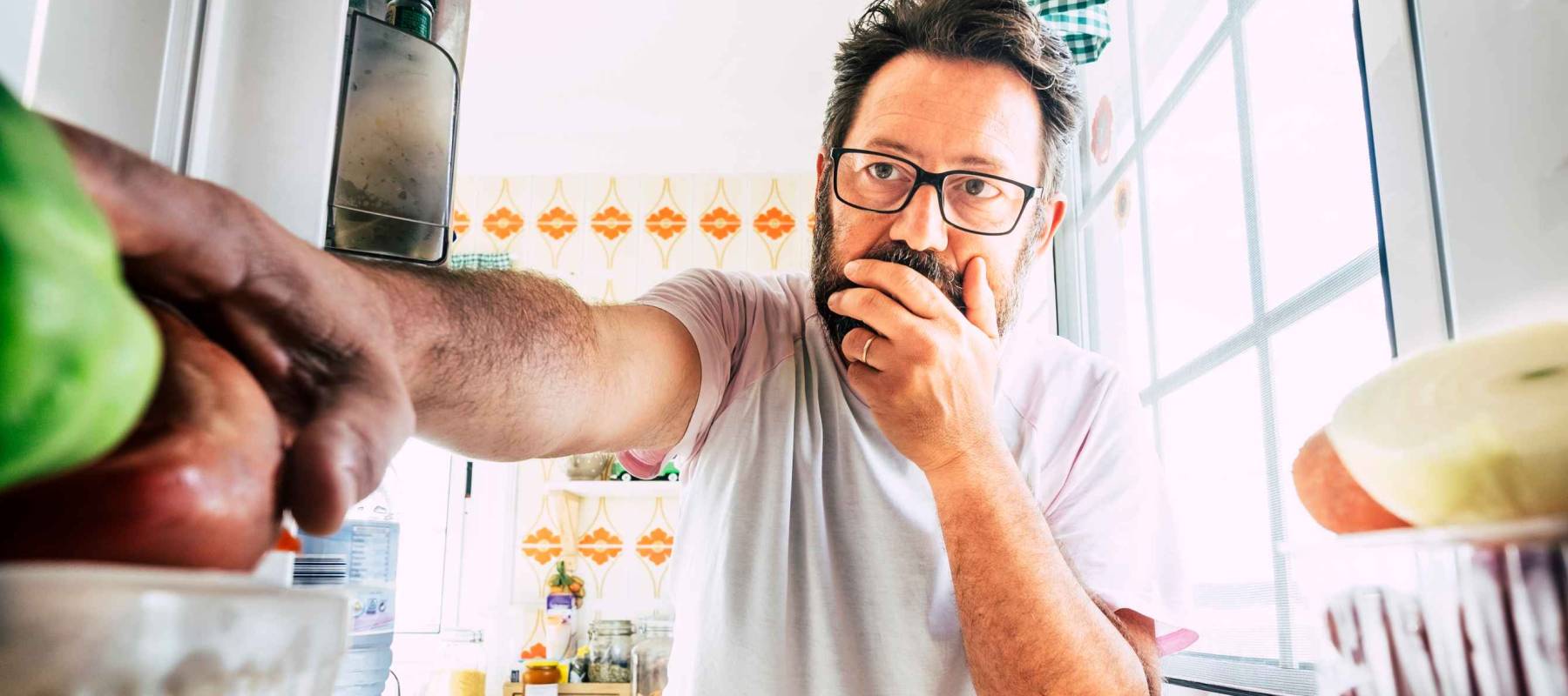 man reaching for food in fridge with face covered