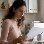 a young woman with long hair looking at documents while sitting at her laptop